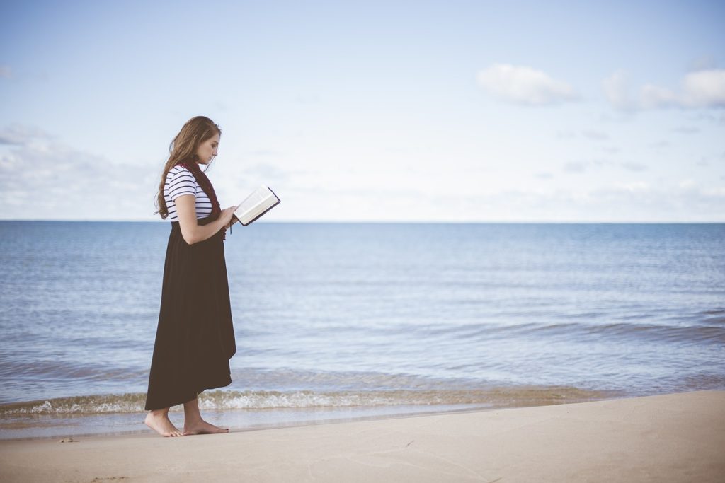 woman reading on beach near ocean