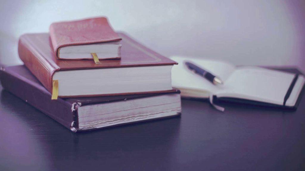 stack of books next to open notebook with pen