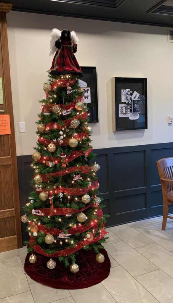 tall Christmas tree decorated with gold balls, red ribbon, and a Victorian angel on top