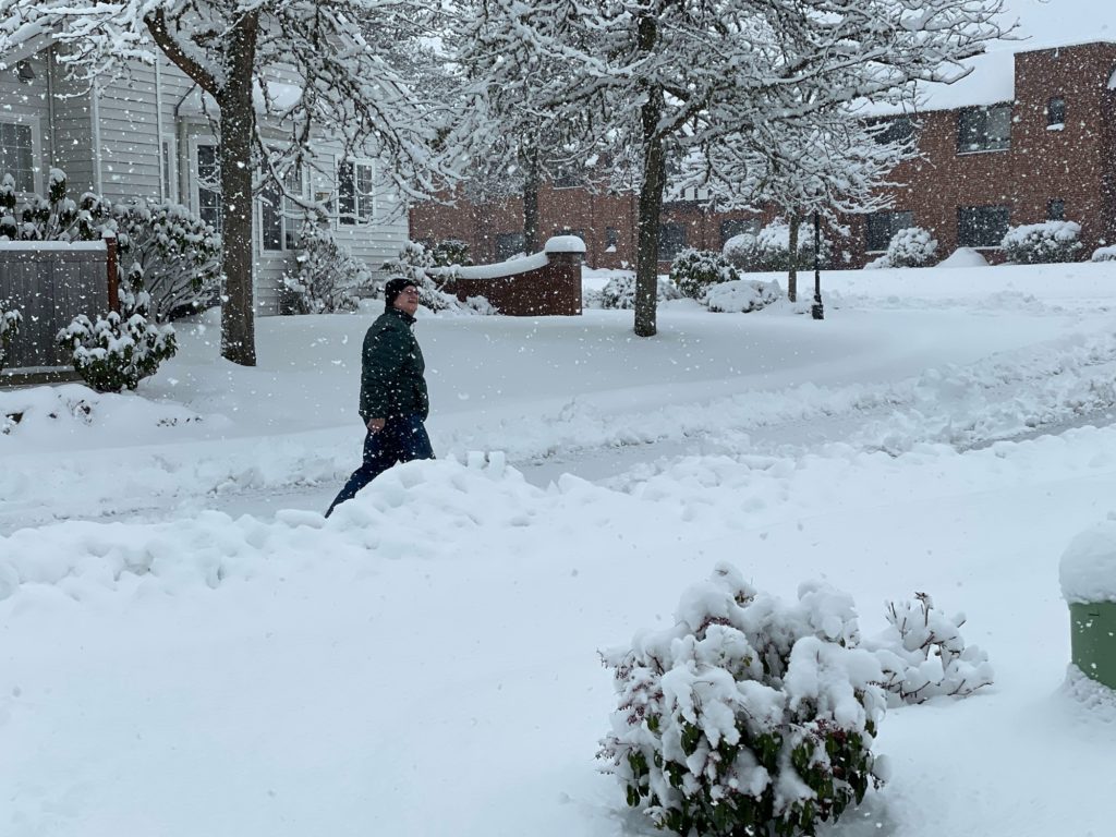 man walking outside through snow as snow continues to fall