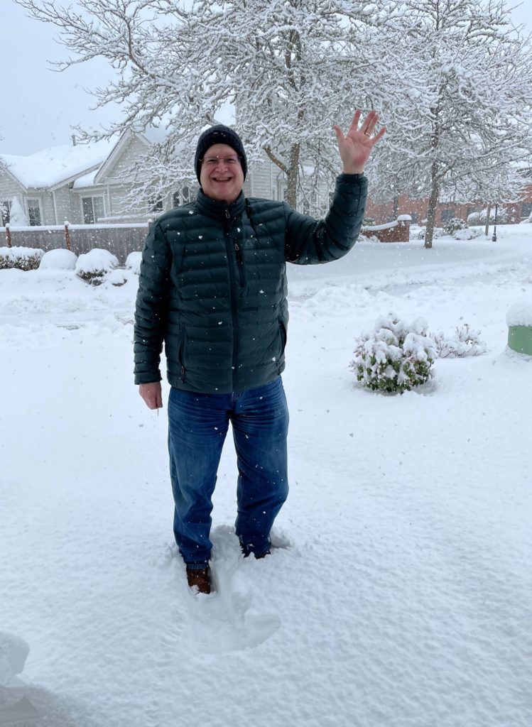 Man standing in snow waving while snow continues to fall