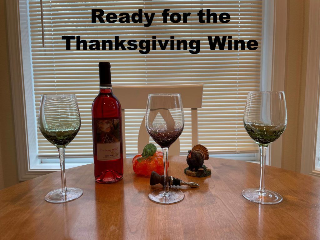 items on a kitchen table: bottle of rose wine, 3 wine glasses, glass pumpkin ornament, ceramic turkey