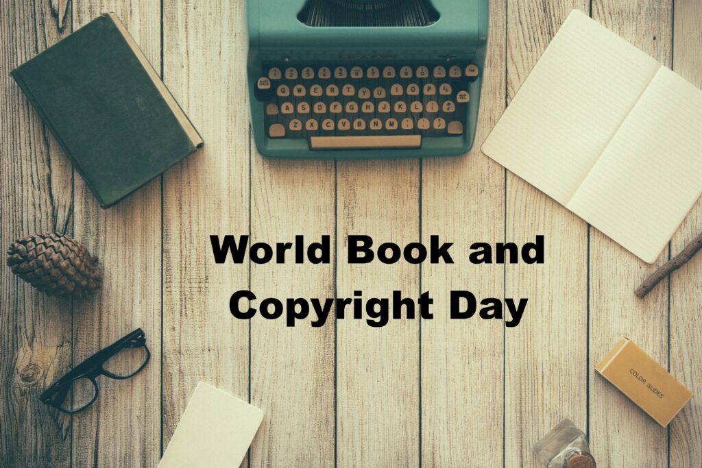 Photo taken from above showing writing tools arranged in a circle: (from top, clockwise) typewriter, bland page spread of open notebook, small writing pad, black-rimmed glasses, pinecone, closed book. Title: World Book and Copyright Day