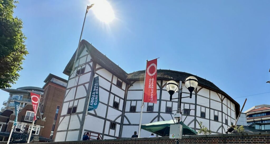 Current Globe Theatre, London, England. A 3-story circular building, white stucco with brown trim and roof.